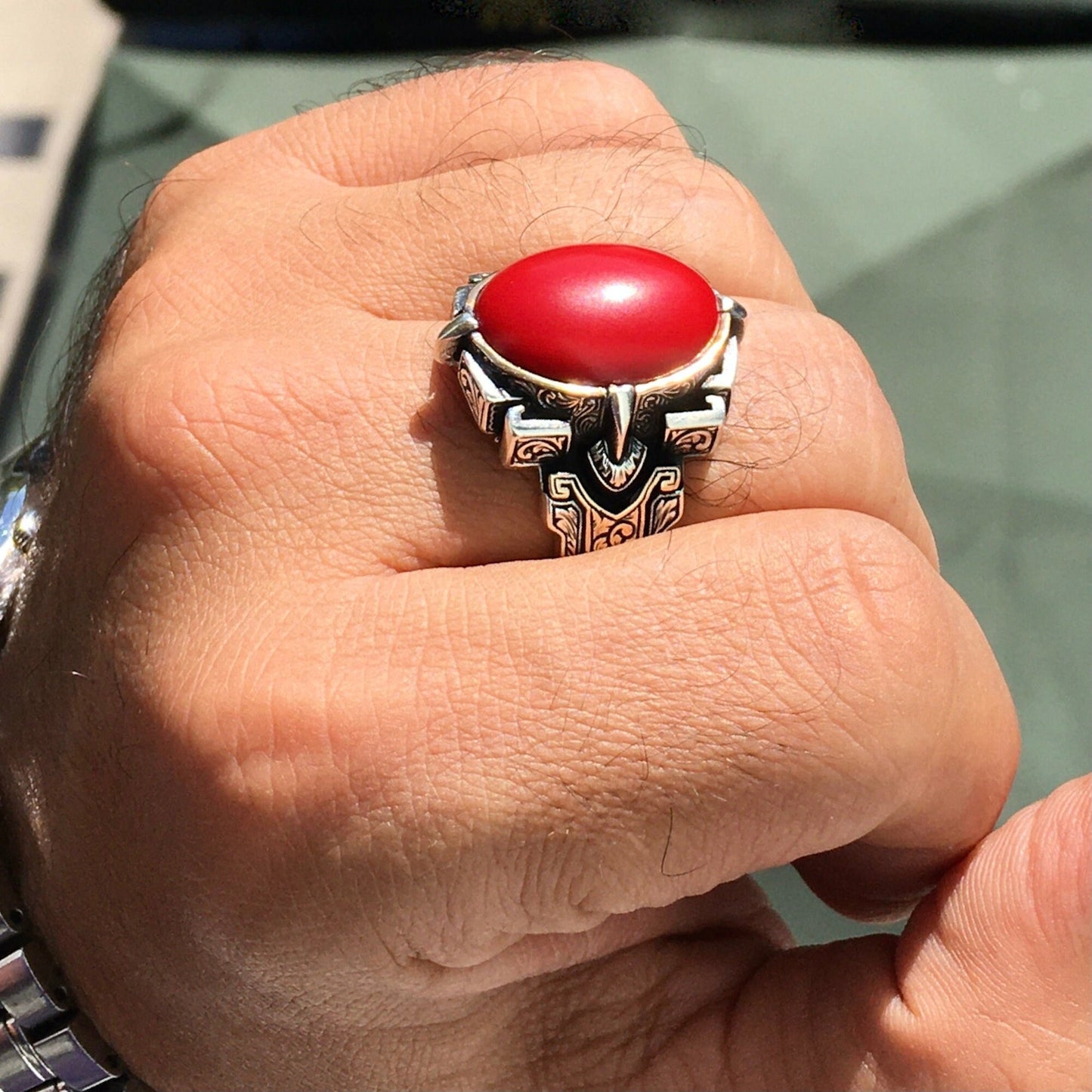 Hand wearing a silver ring with a red stone on a blurred background