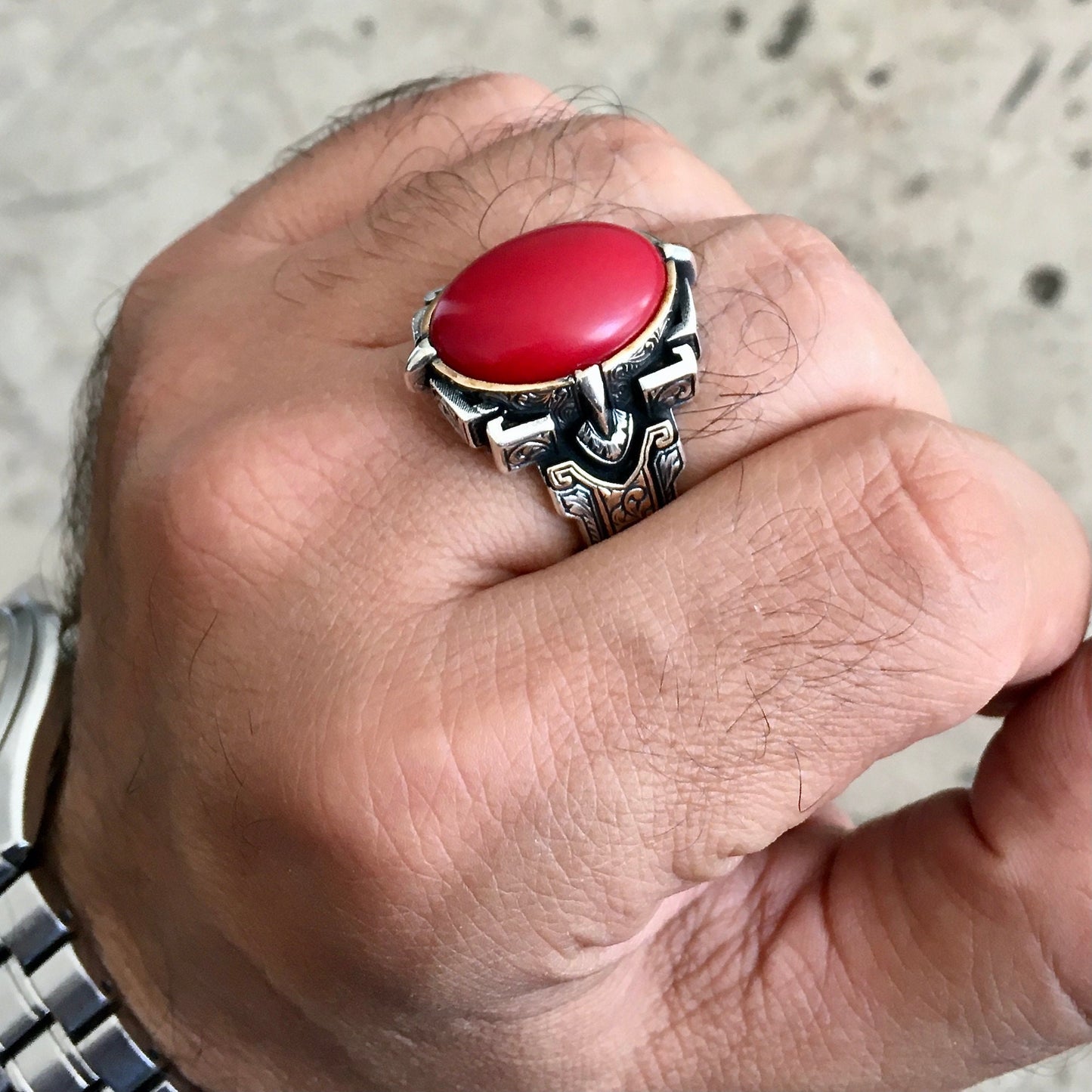 Hand wearing a silver ring with a red stone on a neutral background